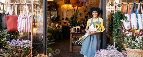 Preview: Florist owner holding sunflowers is smiling in the doorway of her flower shop