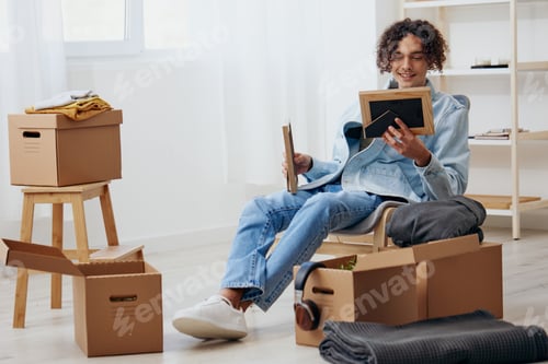 Preview: handsome guy sitting on a chair unpacking with box in hand moving Lifestyle