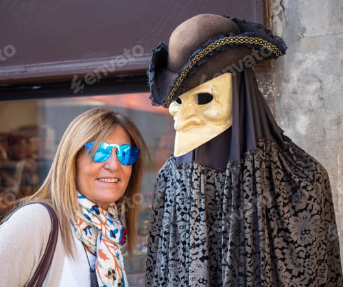 Preview: Woman smiling while posing with a mannequin in a mask shop in Venice.