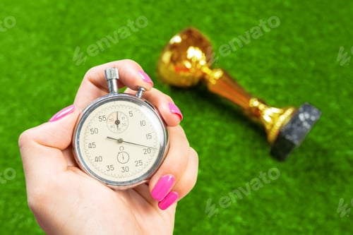 Preview: Holding a stopwatch with a trophy on green grass during a competition