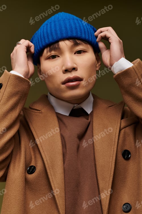 Preview: Stylish Asian man in a trendy outfit poses confidently with a blue beanie in a modern setting