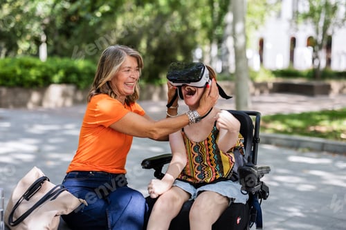 Preview: Happy therapist placing vr headset on young disabled woman in wheelchair outdoors