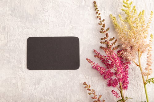 Preview: Black paper business card mockup with purple astilbe flowers on gray concrete background