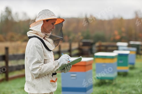 Preview: Middle Aged Beekeeper in Suit Writing in Notepad at Apiary Farm