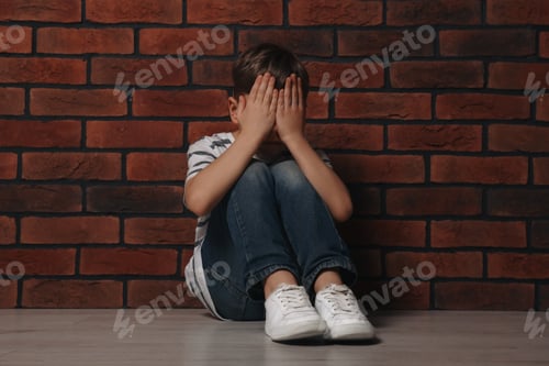 Preview: Upset boy sitting on floor near brick wall. Children's bullying