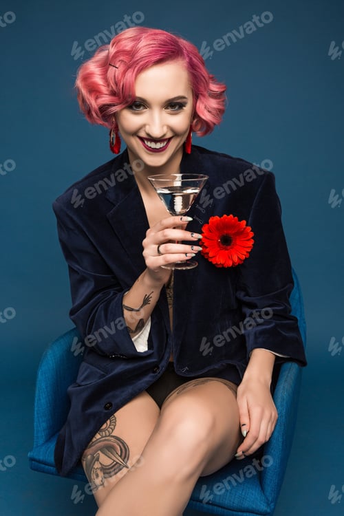 Preview: beautiful tattoed pin up girl in jacket with boutonniere and wineglass infront of blue background