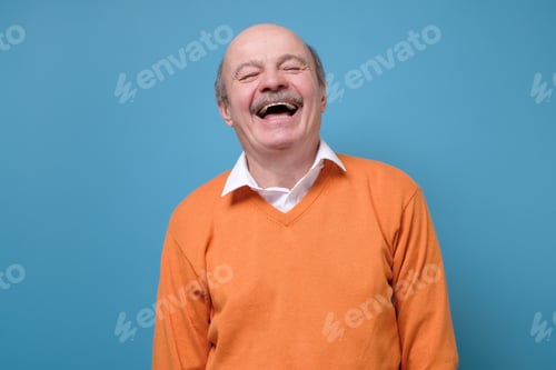 Preview: Senior hispanic man in orange sweater laughing on joke.