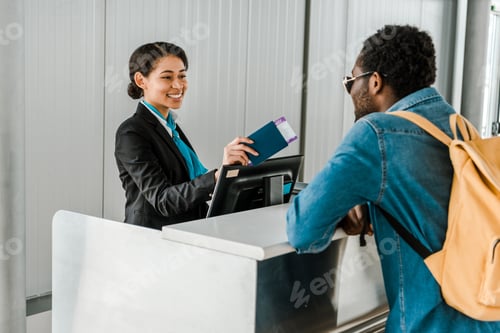 Preview: smiling african american airport worker giving passport and air ticket to tourist with backpack
