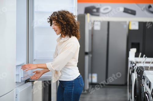 Preview: Woman choosing new refrigerator in electronics store appliance department