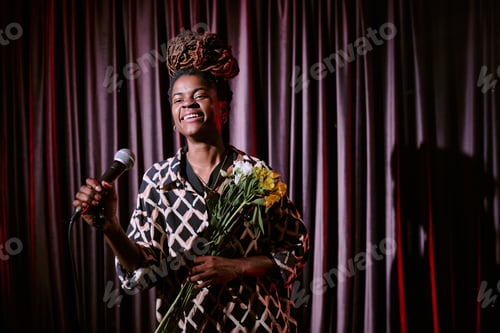 Preview: Smiling Performer Holding Microphone and Flowers on Stage