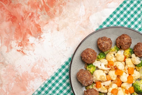 Preview: top half view broccoli and cauliflower salad and meatball on plate green and white checkered napkin
