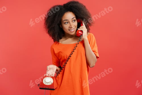 Preview: Portrait of smiling attractive African American woman with curly hair holding landline red phone
