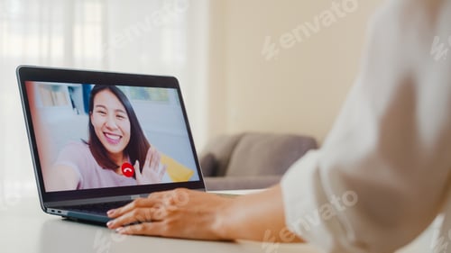 Preview: Young Asian business female using laptop video call talking with friends while working from home