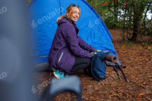 Preview: Female tourist in a forest camping is packing a backpack in preparation for a hike