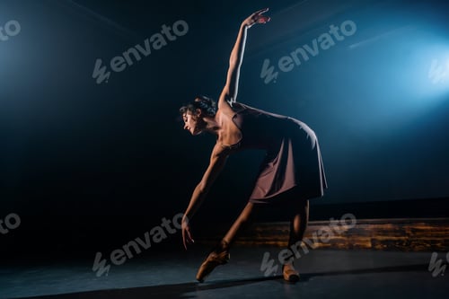 Preview: Graceful ballerina in beige dress dancing elements of classical or modern ballet in dark with