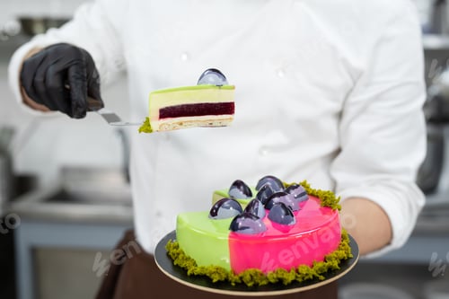 Preview: Close-up of a piece of mousse cake in the hands of a male pastry chef