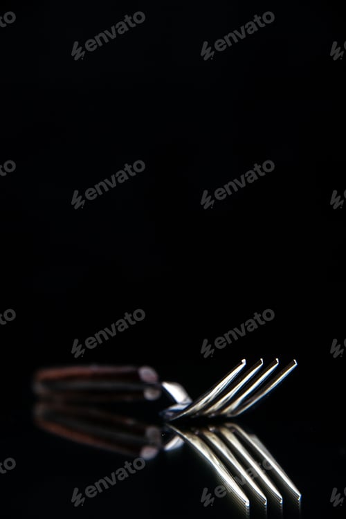 Preview: Blurred view of elegant shiny metal fork on black background with free space in vertical shot