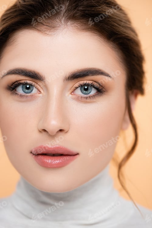 Vista previa: close up portrait of young woman with natural makeup looking at camera isolated on peach