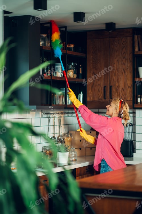 Preview: Housewife cleaning kitchen cabinets with feather duster wearing gloves