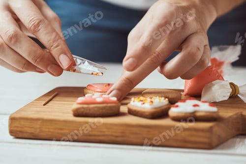 Preview: Decorating gingerbread cookies with icing. Woman hand decorate cookies in shape of heart, closeup
