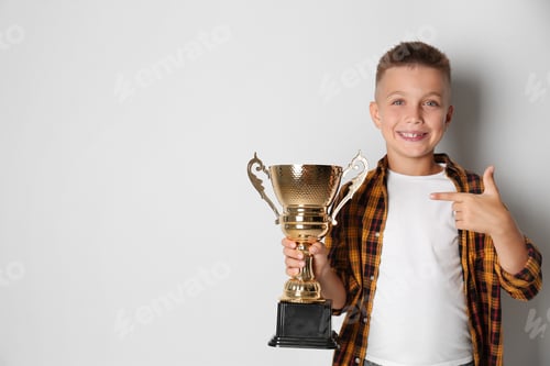 Preview: Happy boy with golden winning cup on light background. Space for text