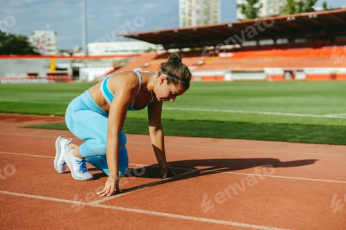 Preview: A track athlete is kneeling in start position on stadium.