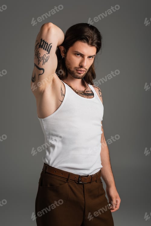 Preview: Muscular and tattooed model in white tank top looking at camera isolated on grey