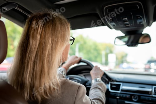 Preview: Woman with blond hair looking through front window while driving for meeting