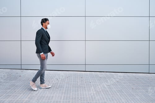 Preview: Businessman with face mask walking outdoors on the street in financial district. Business and urban