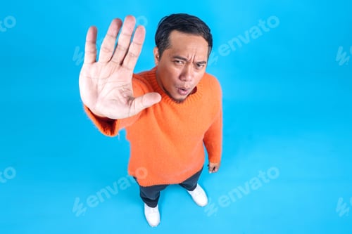 Preview: Full Length High Angle View Of Young Man Saying No Gesture Rejection To Camera On Blue Studio Wall