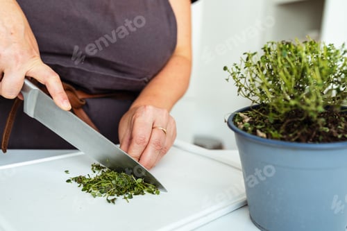 Preview: woman in brown apron cuts herbs on cutting board with sharp kitchen knife