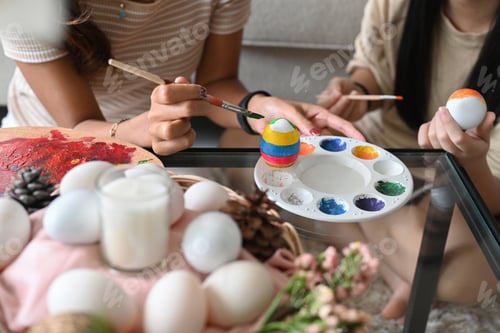 Preview: Child and mother hand painting Easter egg with paintbrush. Easter holidays and people concept.