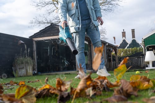 Preview: Man using an electric blower to tidy up leaves in the garden of his home