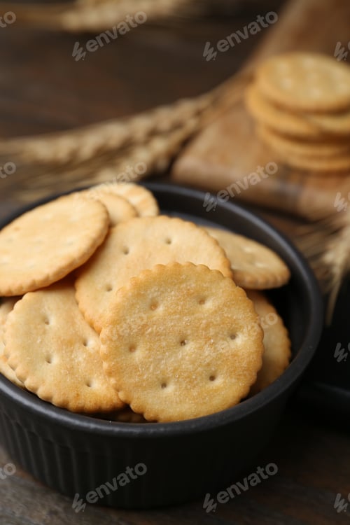 Preview: Tasty salty crackers and wheat spikes on wooden table, closeup