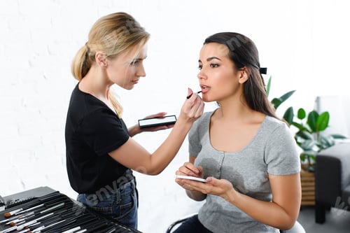 Preview: attractive woman with smartphone getting makeup done by makeup artist