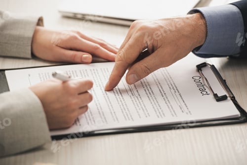 Preview: cropped view of realtor pointing with finger at clipboard with contract lettering near woman