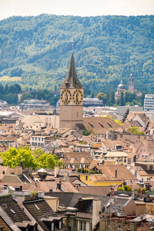 Preview: Historic clock tower overlooking a quaint European town nested amid lush green hills.