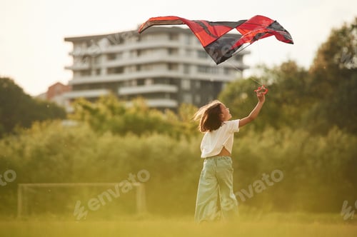 Preview: View from behind. Little girl is playing with kite on the field