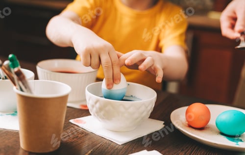 Preview: Easter day. Cropped close up Kid boy hands painting eggs on wooden background. Child sitting in a ki