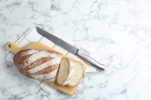 Preview: Wooden cutting board, loaf of bread and knife on white marble table, top view. Space for text