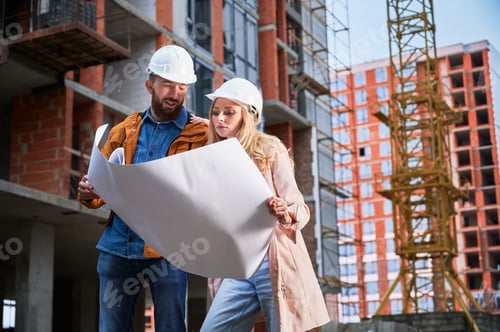 Preview: Man and woman studying building plan at construction site.