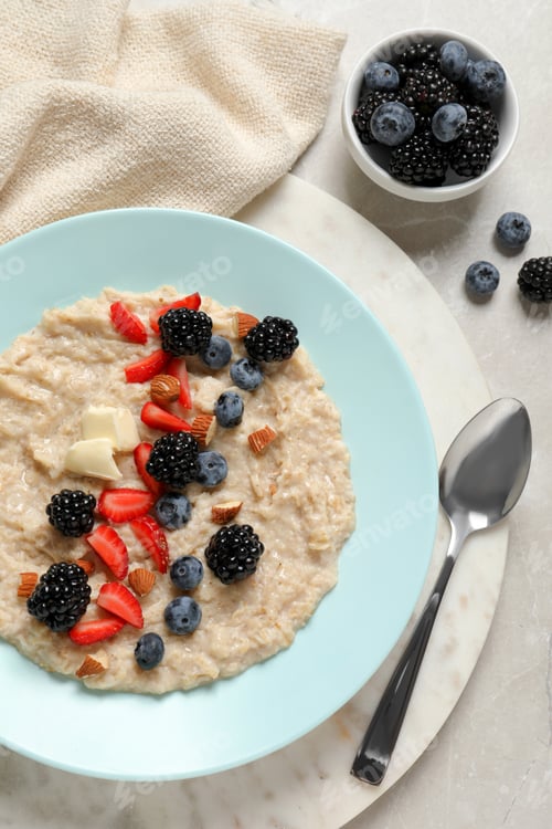 Preview: Tasty oatmeal porridge with berries and almond nuts served on light table, flat lay