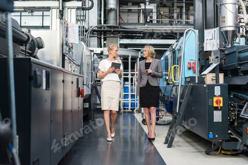 Preview: Two women with tablet walking and talking in factory shop floor