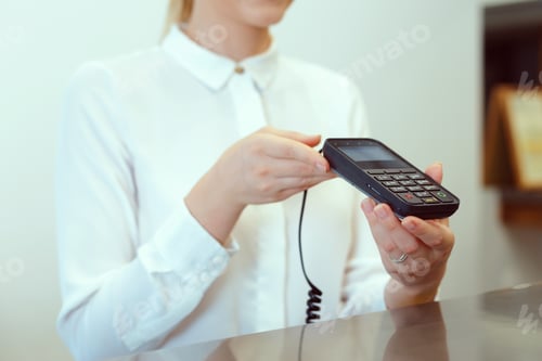 Preview: Woman using a payment terminal at a reception desk in a modern hotel