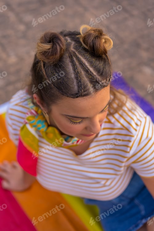 Preview: A vertical shot of a young Caucasian female sitting on LGBT pride flag outdoors