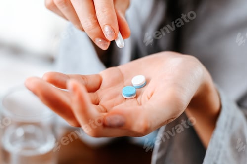 Preview: Businesswomen working at home with glass of water takes white round pill in hand.