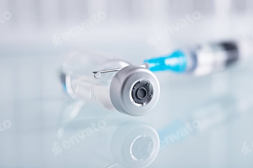 Preview: Closeup shot of a syringe and a closed glass vial with clear liquid on a white surface