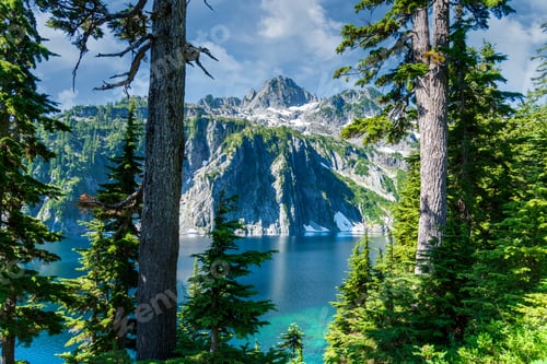 Preview: Alpine lake with jagged rock mountain peaks framed by evergreen pine trees.