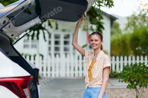 Preview: Woman enjoying a sunny day, standing by an open car trunk, smiling and ready for a fun trip or a