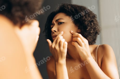 Preview: Young woman checking her skin for acne in the mirror